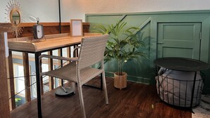 A wooden table with a wicker chair, a potted plant, a wall clock, and a green door. - The Pink Palm - Waterfront - Boat & RV’s Welcome! (Crystal River)