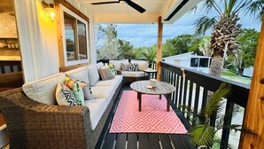 A covered outdoor seating area with a sofa, a small table, and a ceiling fan. - The Pink Palm - Waterfront - Boat & RV’s Welcome! (Crystal River)