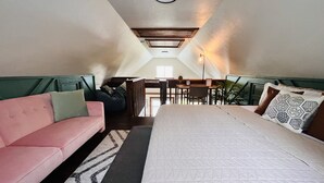 A bedroom with a bed, a pink sofa, a bench, and a dining area with a table and chairs. - The Pink Palm - Waterfront - Boat & RV’s Welcome! (Crystal River)