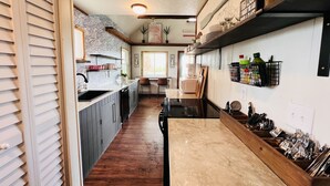 A kitchen with wooden cabinets, a black countertop, and a dining area with a table and chairs. - The Pink Palm - Waterfront - Boat & RV’s Welcome! (Crystal River)