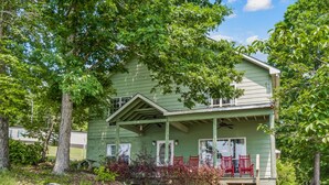 Une maison verte avec un porche et des chaises rouges, entourée d’arbres.