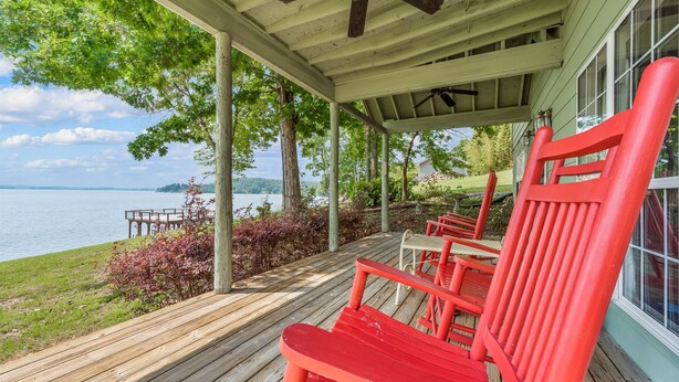 Une véranda avec des chaises rouges, une terrasse en bois et une vue sur un lac.