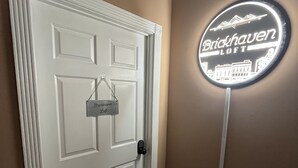 A white door with a nameplate and a neon sign on the wall. - Brickhaven Loft on Historic Main Street - walk to Spring River, State Park, more (Mammoth Spring)