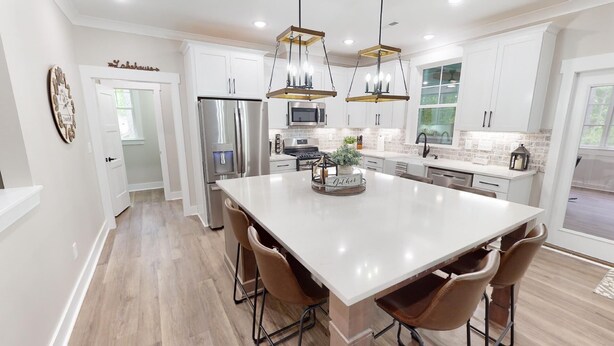 A modern kitchen with white cabinetry, stainless steel appliances, and a central island with bar stools. - Newer property at Kerr Lake with dock! Family-sized with game room and lg porch! (Manson)