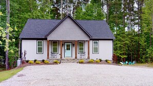 A two-story house with a grey exterior, a dark roof, and a front porch with two chairs. - Newer property at Kerr Lake with dock! Family-sized with game room and lg porch! (Manson)