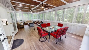 A spacious room with a glass dining table surrounded by red chairs, a ceiling fan, and large windows offering a view of the outdoors. - Newer property at Kerr Lake with dock! Family-sized with game room and lg porch! (Manson)