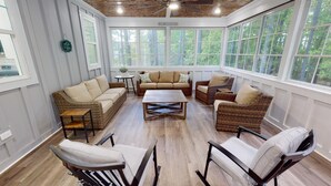 A sunroom with wicker furniture, large windows, and a ceiling fan. - Newer property at Kerr Lake with dock! Family-sized with game room and lg porch! (Manson)