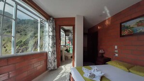 Ein Hotelzimmer mit großem Fenster, einem Bett mit gelber Bettdecke und Blick auf eine gebirgige Landschaft.
