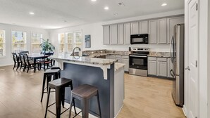 A modern kitchen with a central island, stainless steel appliances, and a dining area with bar stools.