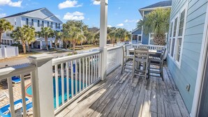A wooden deck with a pool, a covered seating area, and a view of neighboring houses.
