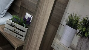 Une chambre moderne avec une tête de lit en bois, une table de chevet agrémentée d’une plante et un luminaire mural formant le mot « HOME ».
