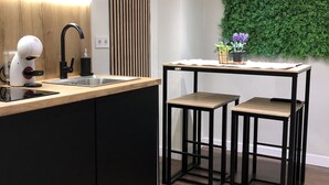 Une cuisine moderne avec un plan de travail en bois, des meubles noirs et un mur vert. On y trouve deux tabourets et une petite table avec une plante.