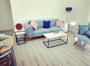 A modern living room with a light blue sofa, a white coffee table, and a blue armchair.