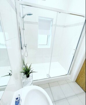 Casa de banho moderna com cabine de duche em vidro, lavatório branco e planta em vaso.