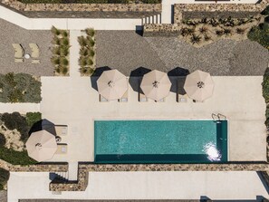 Vista aérea de una zona de piscina con sillas de descanso y sombrillas.