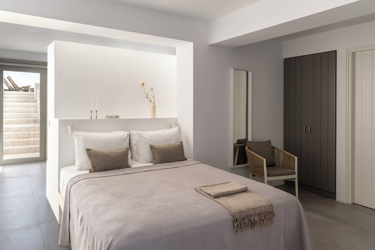 A modern bedroom with a large bed, a chair, a wardrobe, and a mirror.