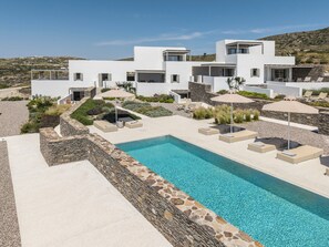 A modern poolside area with a clear blue pool, stone walls, and outdoor seating. - Korfi de Milo (Milos)