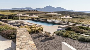 A pool area with lounge chairs and umbrellas, surrounded by landscaped gardens and a view of distant mountains. - Korfi de Milo (Milos)