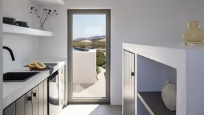 A modern kitchen with a view of the outdoors, a white countertop, and a door leading to a balcony. - Korfi de Milo (Milos)