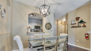 A dining area with a wooden table and chairs, a hanging light fixture, and a clock on the wall.