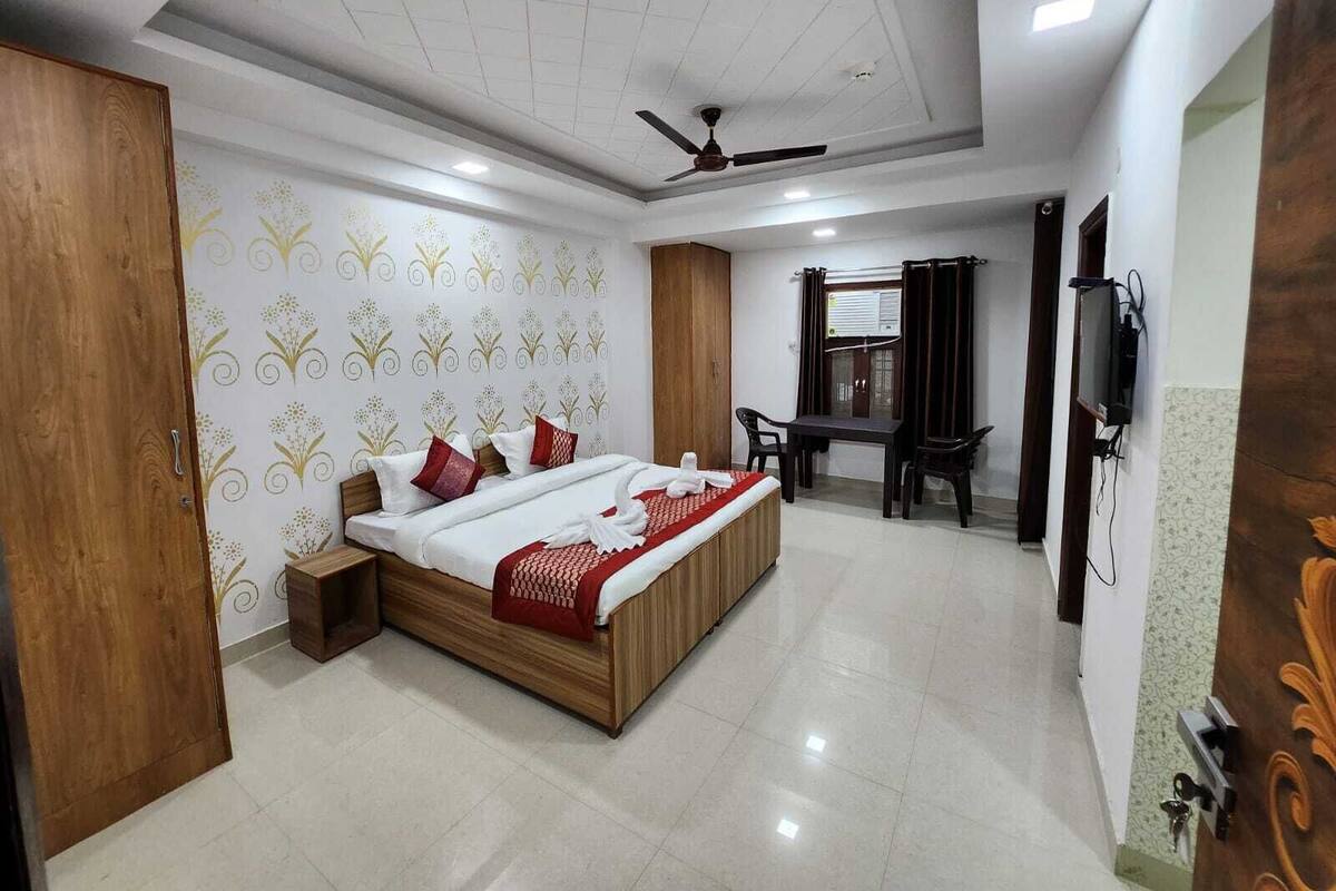 A bedroom with a bed, a desk, a chair, a television, and a ceiling fan.