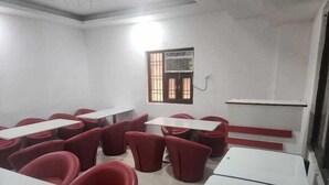 A classroom with red chairs and white tables, a window with bars, and a whiteboard. - Hotel Abode Inn (New Delhi)