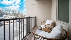 Un balcon avec des fauteuils en osier et une vue sur un parking et des maisons.