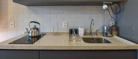 A kitchen with a microwave, kettle, coffee maker, and a sink.
