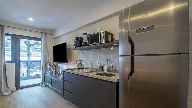 A modern kitchen with stainless steel appliances, a flat-screen TV, and a large window with a view of the outside. - 4 Minutes From Ipanema Beach Fa202 (Rio de Janeiro)