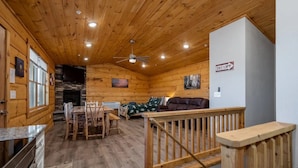 A cozy cabin interior with a dining area, a sofa, and a staircase.