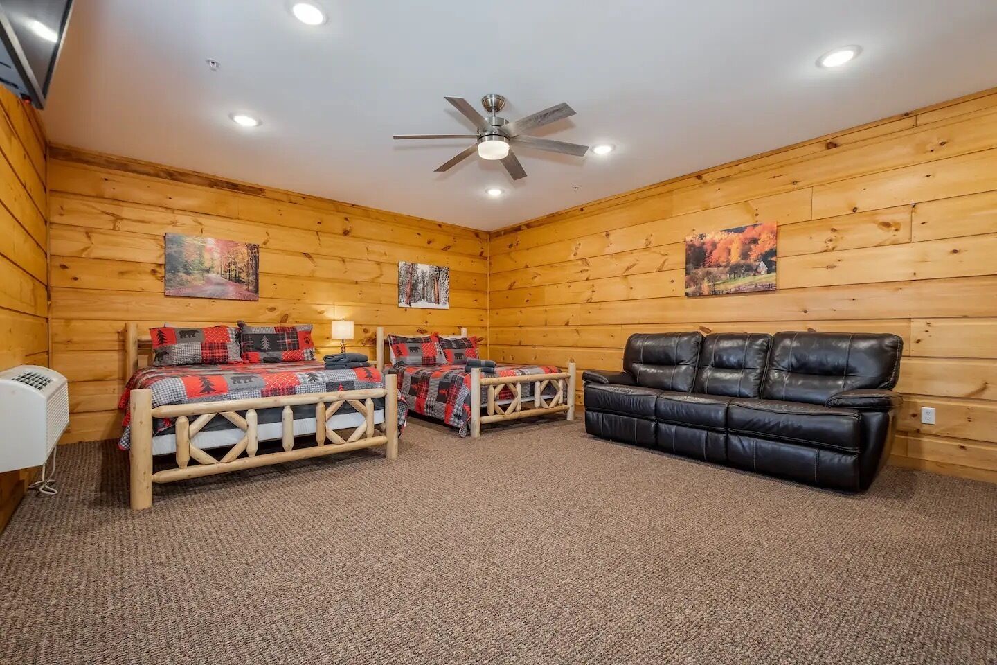 A log cabin room with two wooden beds, a black leather sofa, and a ceiling fan.