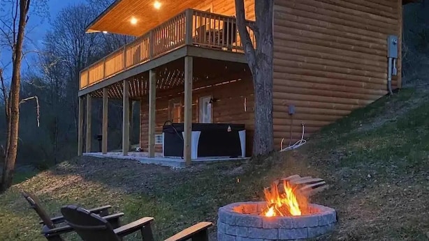A log cabin with a covered porch, a fire pit, and outdoor seating.