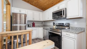 A kitchen with white cabinets, stainless steel appliances, a wooden ceiling, and a granite countertop.