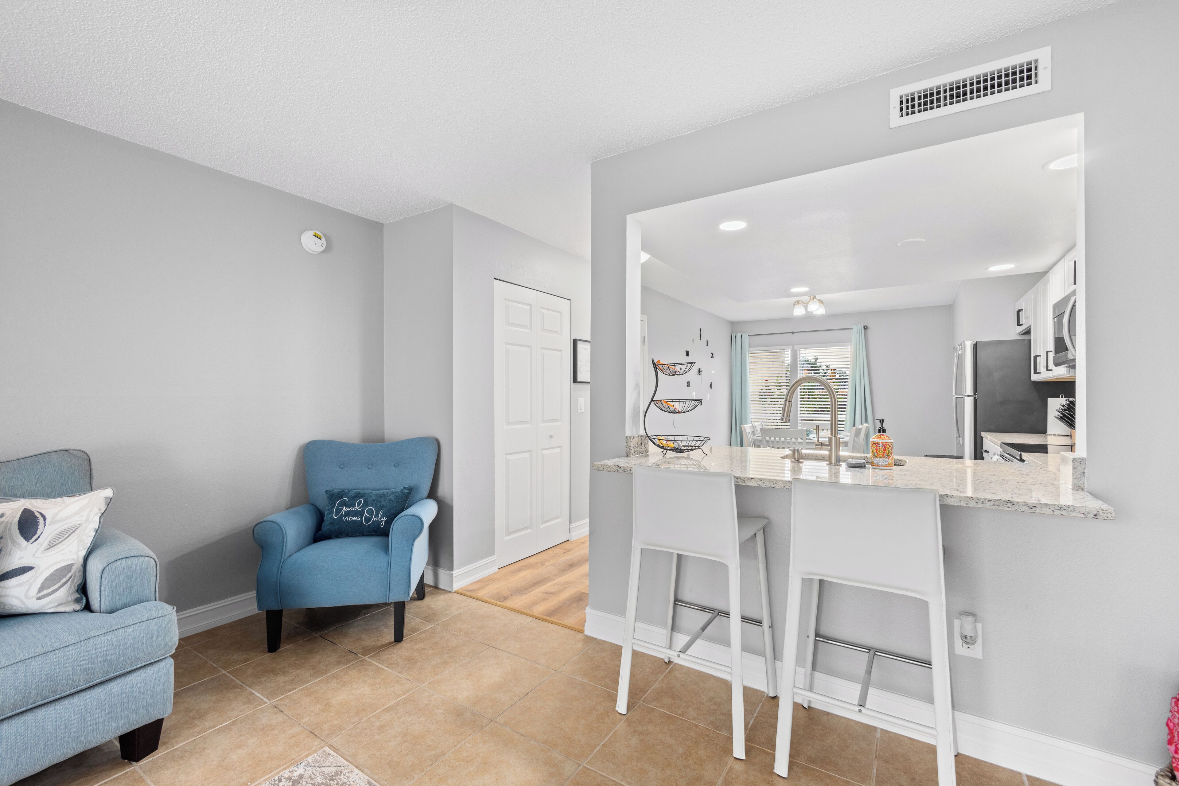 A modern kitchen with a bar area, a blue armchair, and a white door.