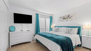 Ein Schlafzimmer mit Bett, Wand-TV, Nachttisch mit Lampe und Fenster mit Vorhängen.