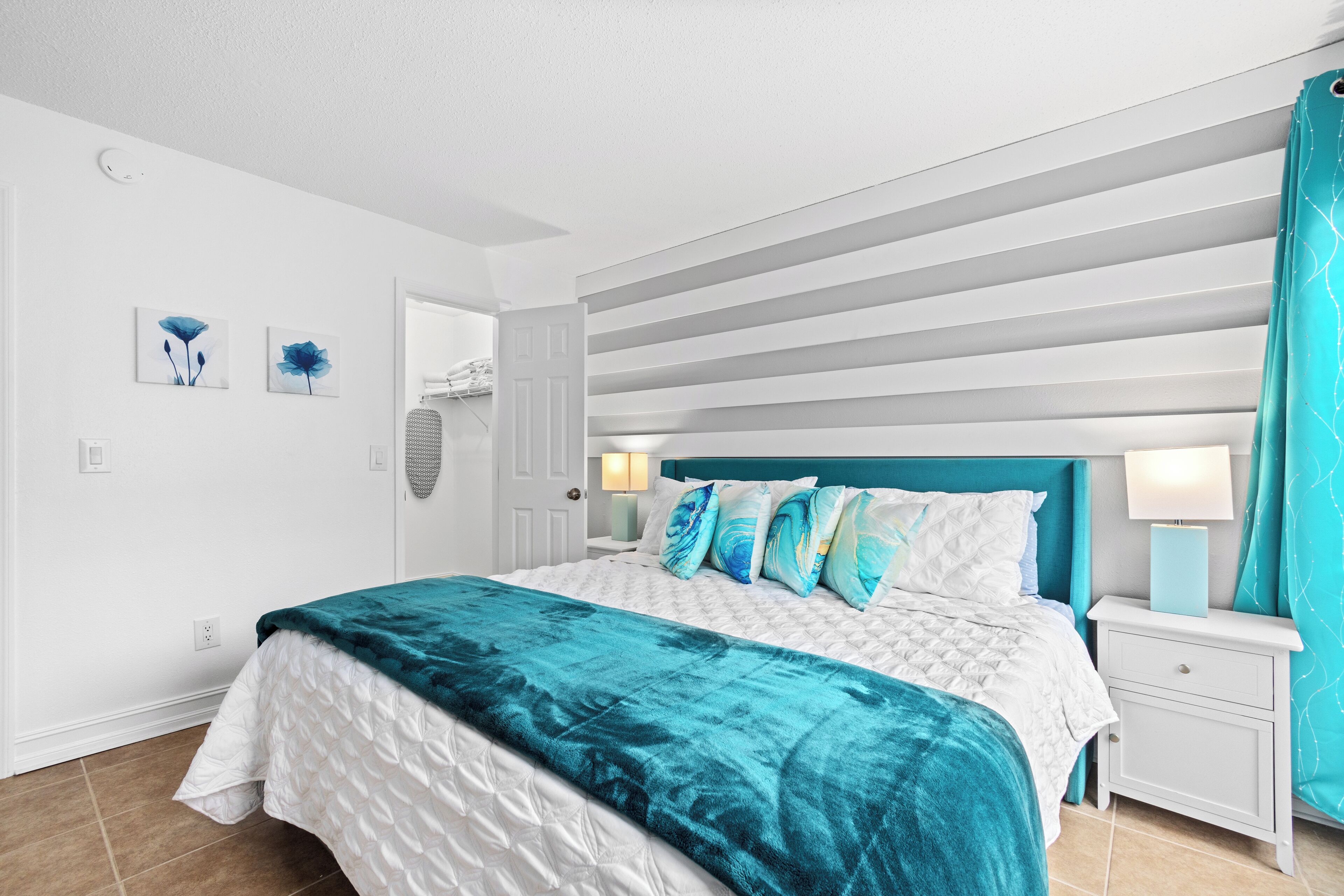 A bedroom with a bed, a nightstand, a door, and a wall with two framed pictures.