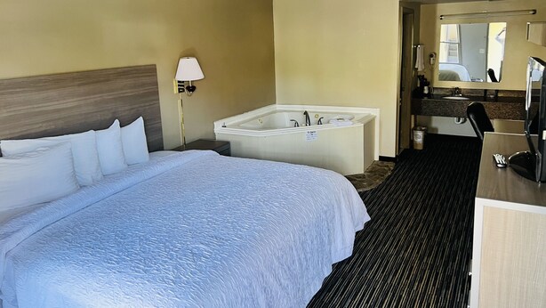A hotel room with a large bed, a separate bathroom with a bathtub, a desk, and a mirror. - Alpine Valley Inn (Helen)