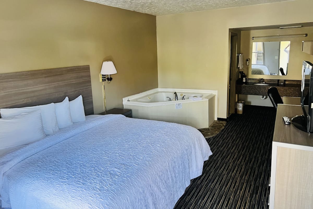 A hotel room with a large bed, a separate bathroom with a bathtub, a desk, and a mirror.