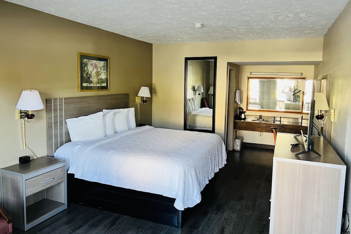 A hotel room with a bed, bedside tables, a mirror, a dresser, and a bathroom visible through an open door.