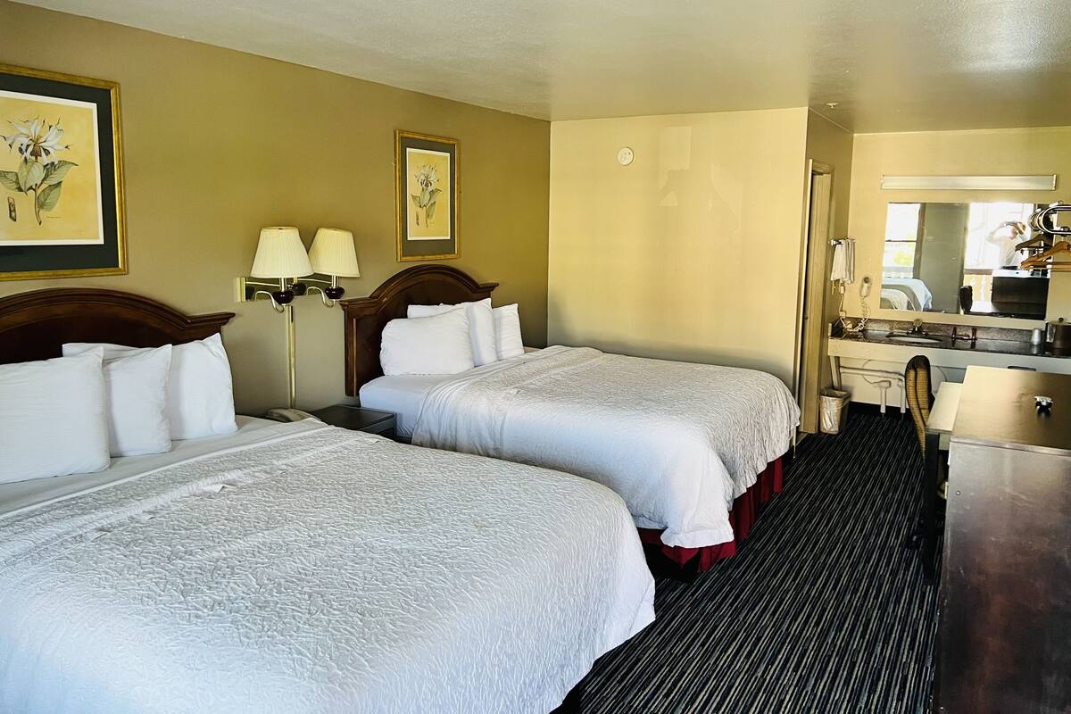 A hotel room with two beds, a desk, a mirror, and a bathroom.