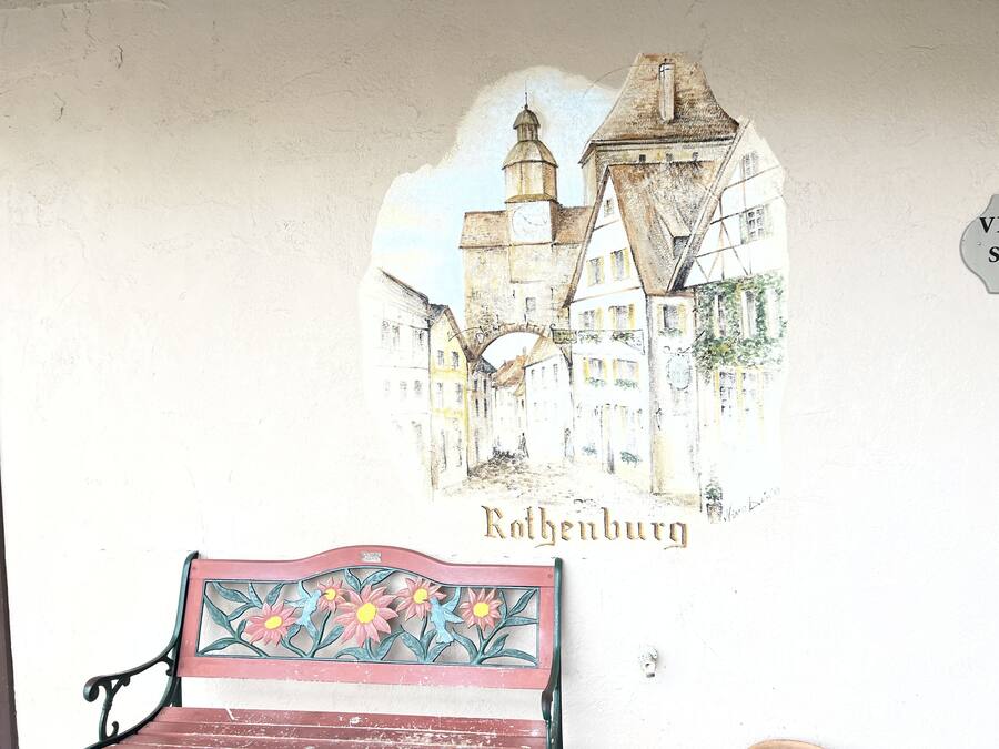 A wall with a mural of a town and a bench.