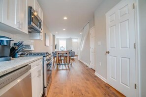 A modern kitchen with white cabinetry, a built-in stove, and a dining area with a table and chairs.