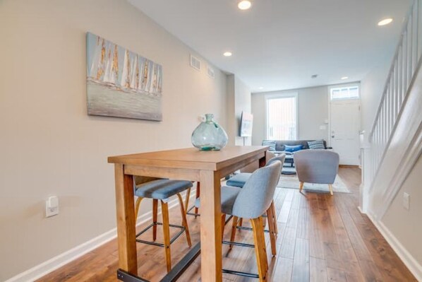 A dining area with a wooden table and bar stools, a painting on the wall, and a staircase leading to another room.