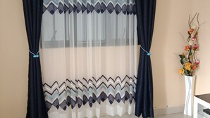 Una habitación con ventana cubierta por una cortina translúcida y un cortinaje estampado.