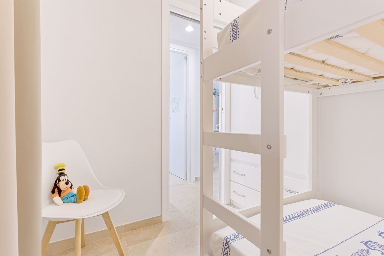 A child's room with a bunk bed, a white chair with a plush toy, and a white wardrobe.