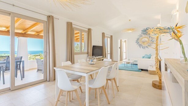 A modern, open-plan living space with a dining area, a sofa, and a view of the sea. - Villa with beautiful sea view (Tertenia)