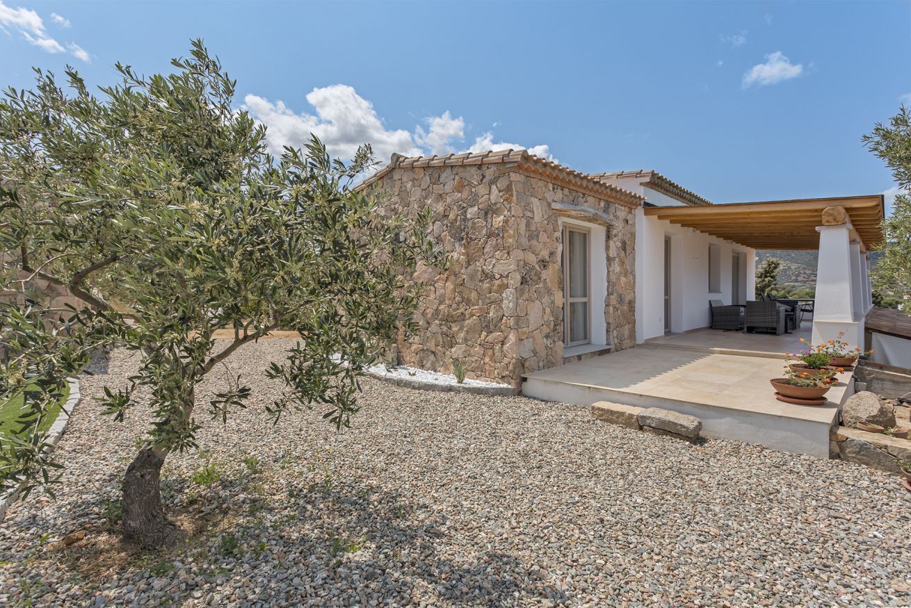 Un edificio de piedra con techo de tejas, camino de grava y una pérgola.