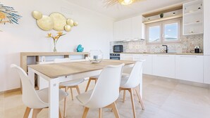 A modern kitchen with white cabinets, a wooden dining table, and white chairs. - Villa with beautiful sea view (Tertenia)