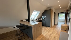 A modern kitchen with a wooden island, black bar stools, a built-in oven, and a large window providing natural light.