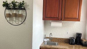 A compact kitchen with wooden cabinets, a granite countertop, a stainless steel sink, and a coffee maker. - Escape By The Bay (Tampa)